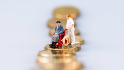 Figurka niepełnosprawnego i jego opiekuna na stosie pieniędzy