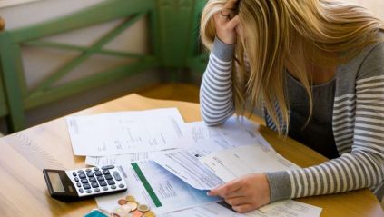 Smutna kobieta siedząca nad rachunkami z kalkulatorem