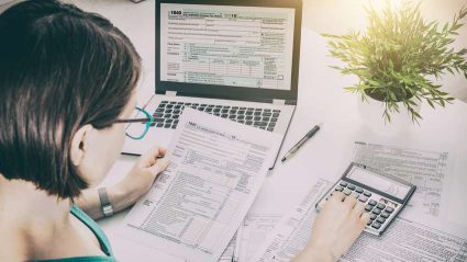 Kobieta siedząca przy komputerze z kalkulatorem i dokumentami finansowymi