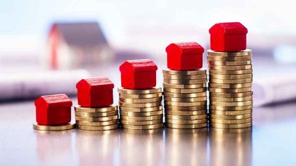 Ceny mieszkań symbolizowane przez modele domków stojące na stosach pieniędzy