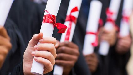 Studenci z rulonami papieru przewiązanego czerwoną wstążką