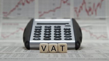 Napis VAT na tle kalkulatora i wykresów