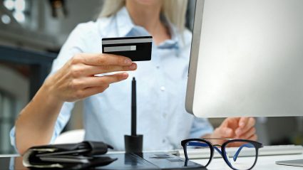 Kobieta siedząca przy komputerze z kartą płatniczą i portfelem
