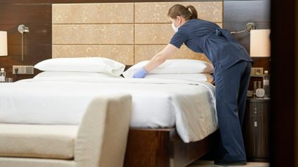 Pokojówka sprzątająca pokój w hotelu w maseczce ochronnej i rękawiczkach