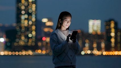 kobieta trzymająca smartfon na tle panoramy miasta