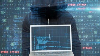 Haker w kapturze trzymający laptopa z napisem cyberatak