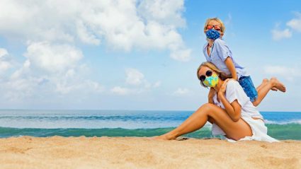 Matka i dziecko na plaży w maseczkach ochronnych przeciwko COVID-19