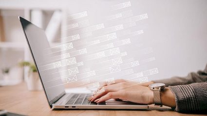 Poczta elektroniczna, człowiek siedzący przy klawiaturze laptopa, symbole e-maili wylatujące z ekranu