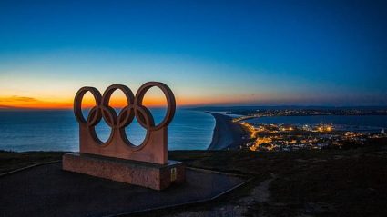 5 kół, symbol olimpijski na tle krajobrazu i zachodzącego słońca