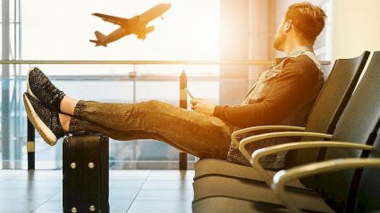 wakacje, mężczyzna siedzący w poczekalni na lotnisku, samolot za oknem