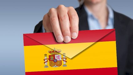 młody człowiek trzymający w dłoni kopertę w barwach flagi Hiszpanii