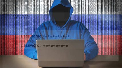 człowiek w kapturze, bez twarzy, piszący na laptopie, na tle wirtualnej flagi Rosji