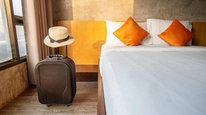 pokój hotelowy, łóżko, walizka, kapelusz słomkowy