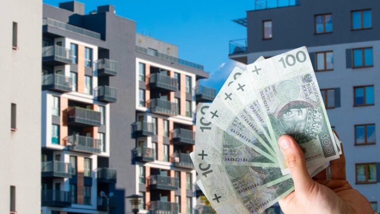 bloki mieszkalne, dłoń z plikiem banknotów 100 zł